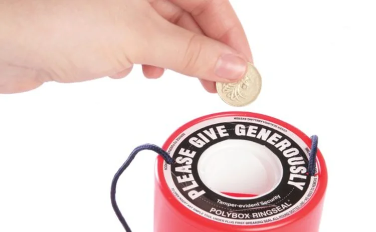A pound coin being placed into a charity tin