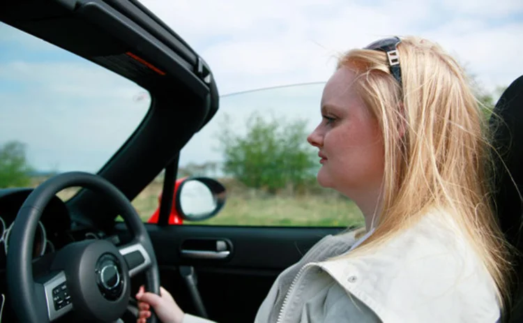 A young lady driving a car with the roof down