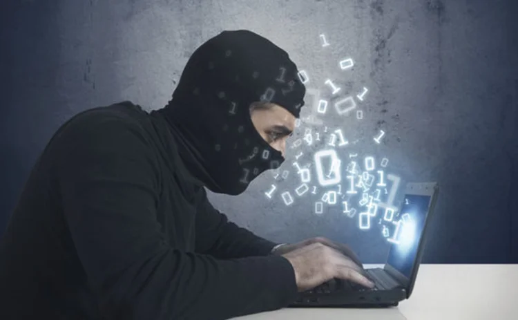 A criminal in a balaclava hacking into a laptop computer