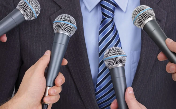 Microphones being held up to a man in a suit