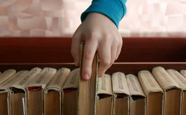 Close-up of a child's hand taking a book from a book shelf