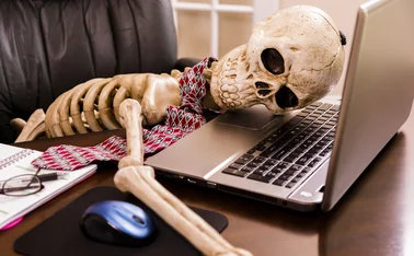 Skeleton of a man with head on laptop in his office. This dedicated employee has worked himself to death!