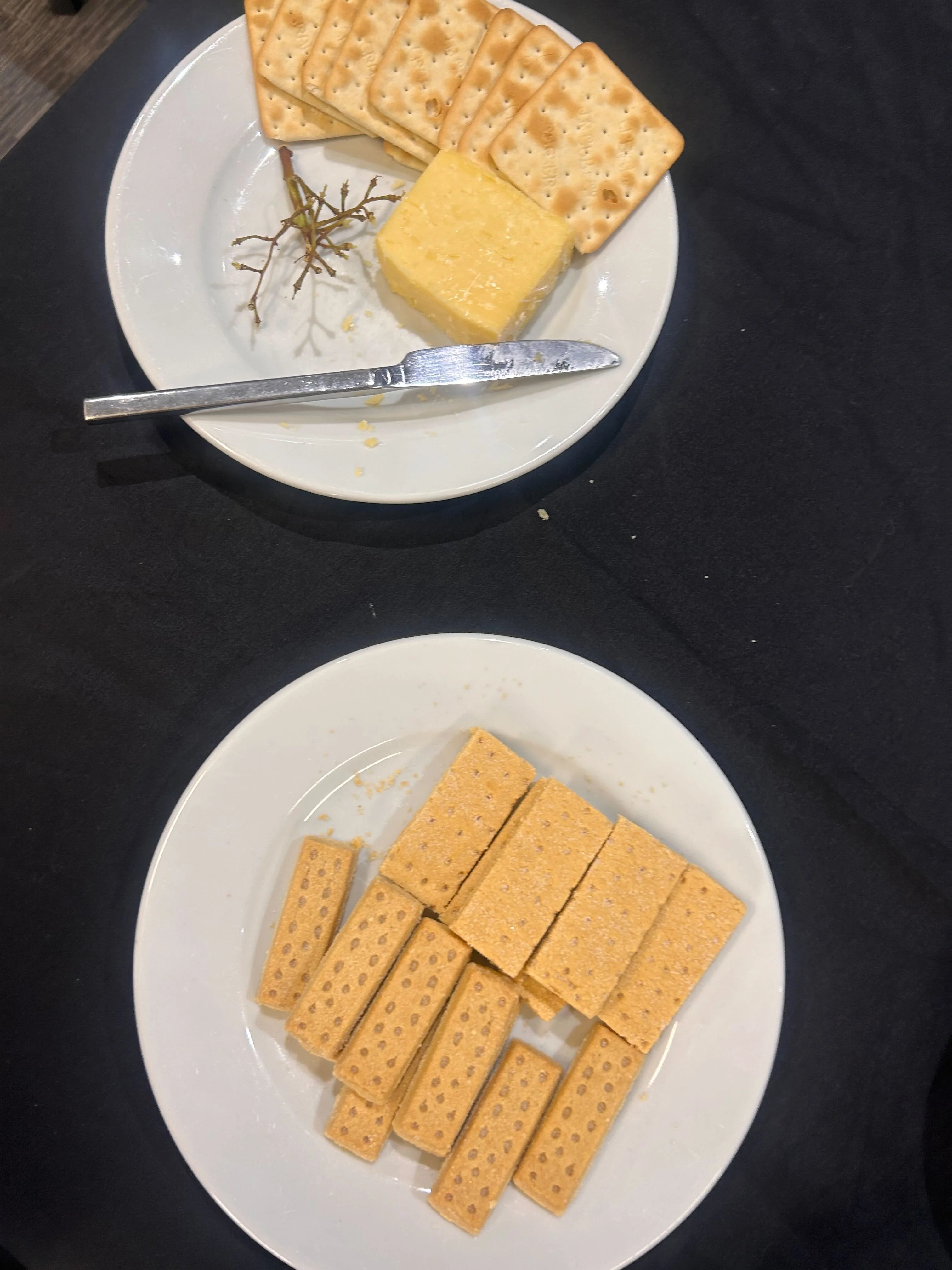 Two white plates of cheese, crackers and shortbread.