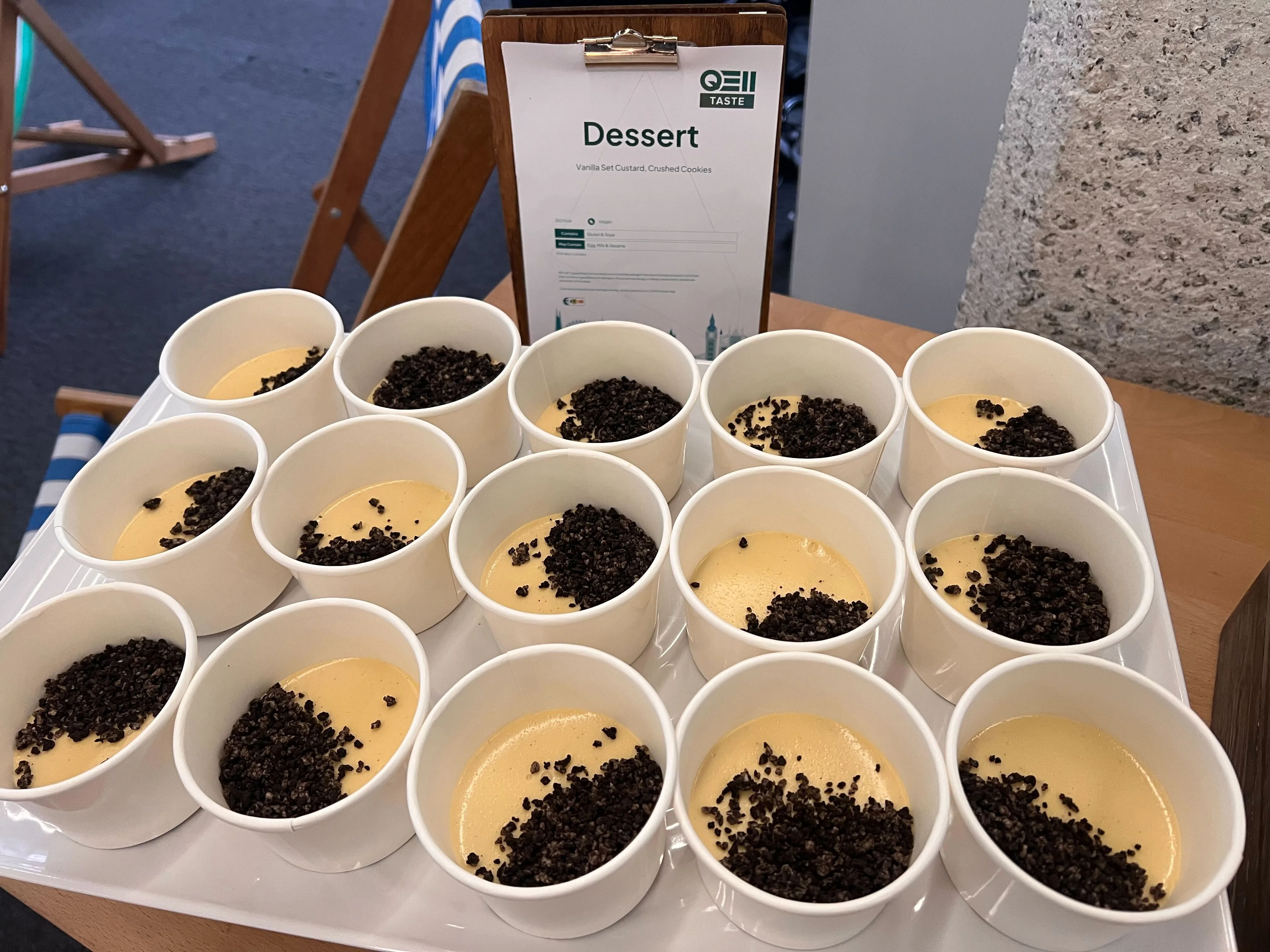 A tray of vanilla set custard with crushed cookies in round paper bowls.