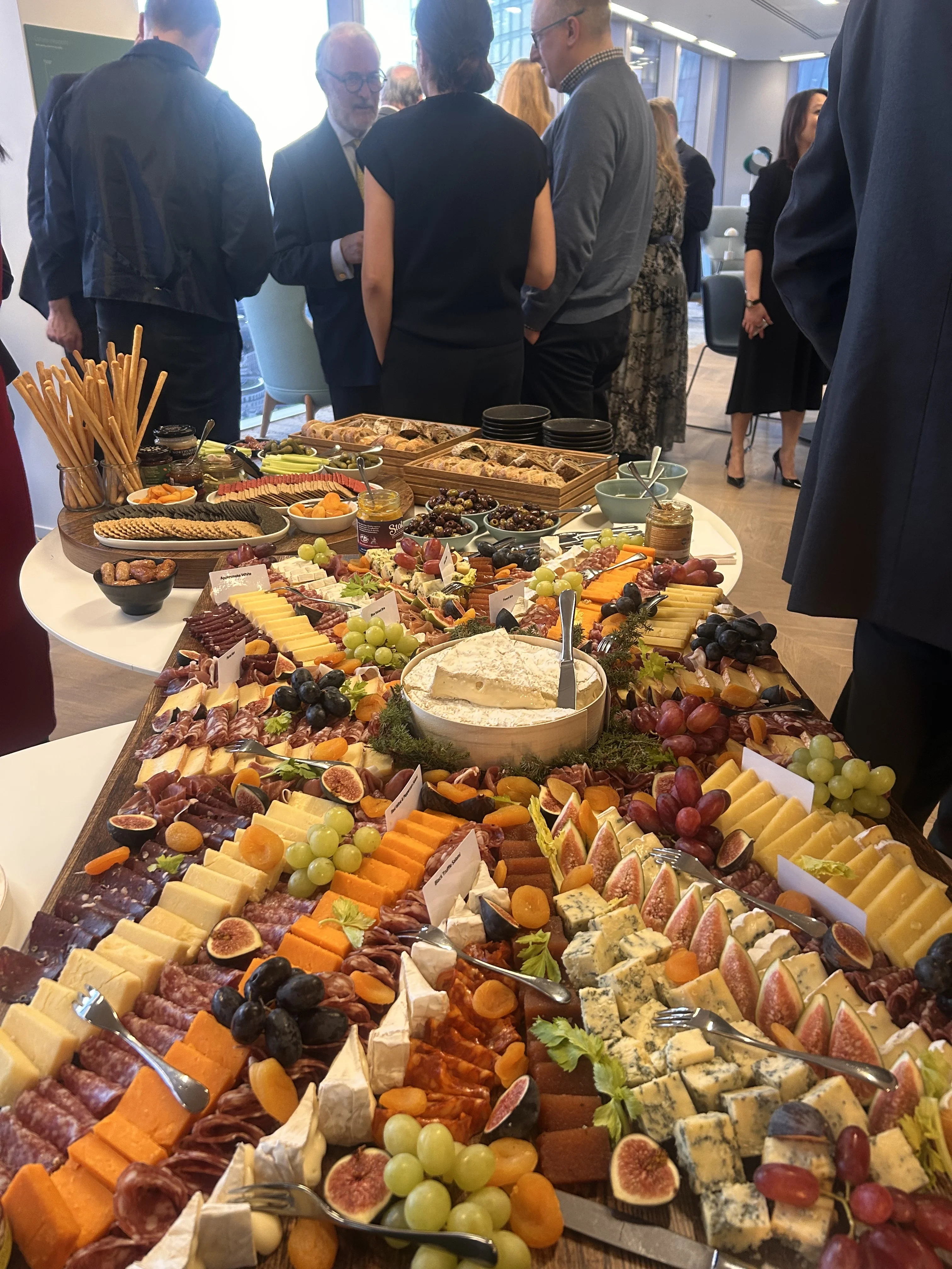 A long wooden tray with cheese, fruit and meats laid out in an aesthetically pleasing manner.