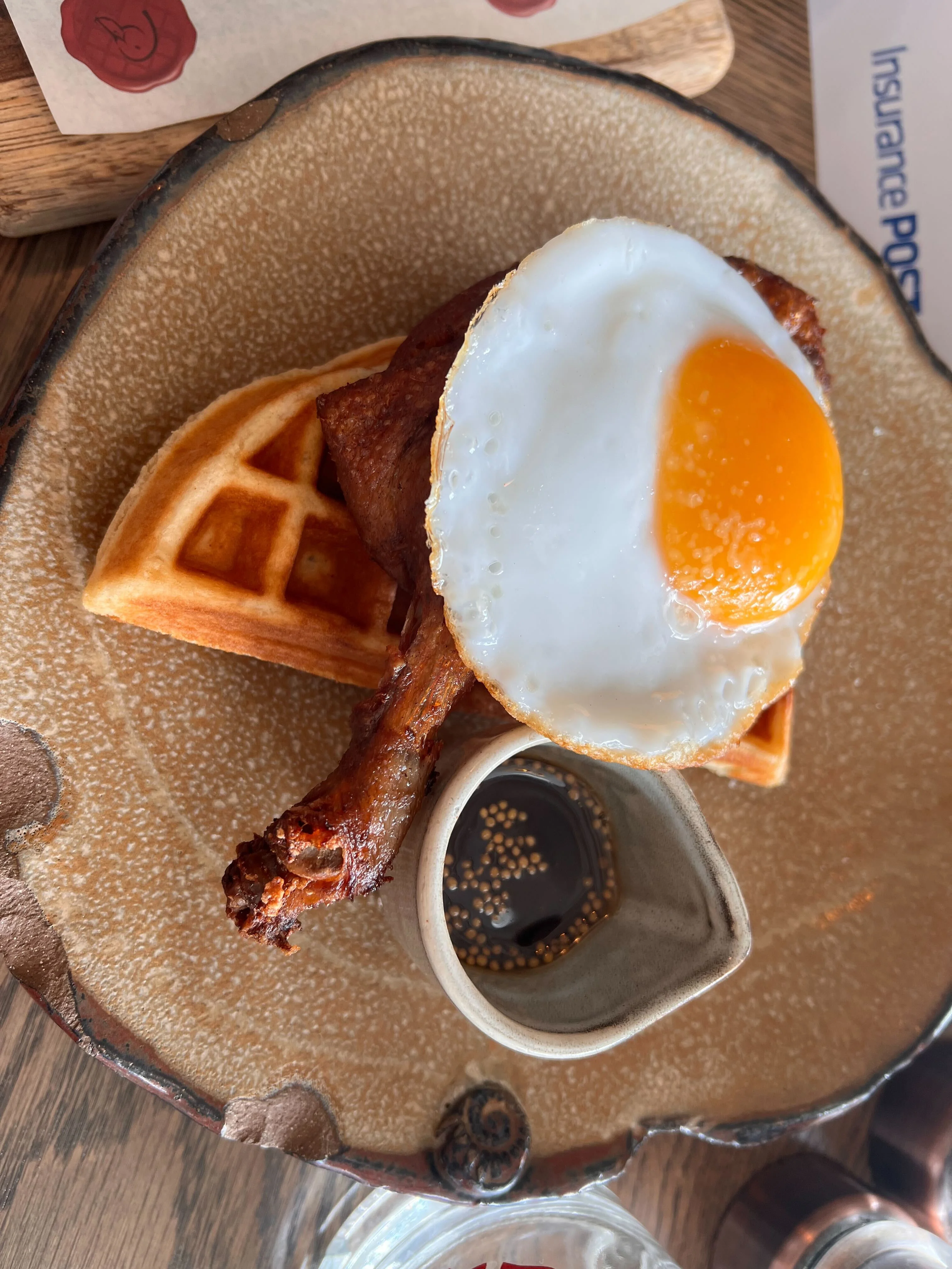 Gressingham duck crispy leg confit, fried duck egg, mustard maple syrup on a tan plate.