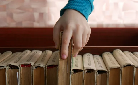 Close-up of a child's hand taking a book from a book shelf