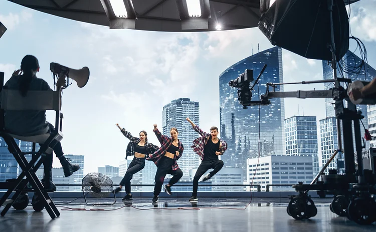 Music Clip Studio Set: Shooting Hip Hop Video Dance Scene with Three Professionals Dancers Performing on Stage with Big Led Screen with Modern City Background. Director and Cameraman in Backstage