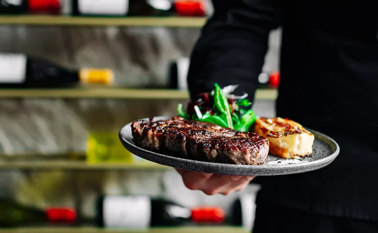 chef in black uniform holds plate of steak dinner
