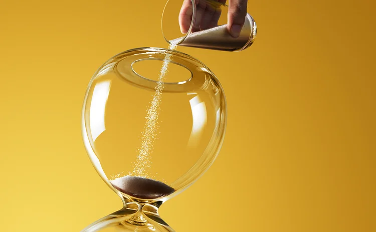 A hand pouring more sand into a hourglass.