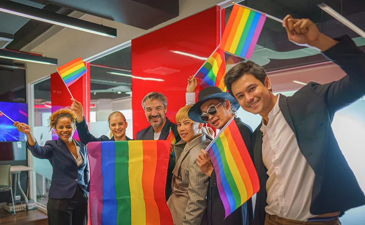 Diverse group of business people (man, woman, gay, transgender, lesbian, asian, caucasian, african american, lgbtq) with rainbow flag on hand combine together as teamwork in office