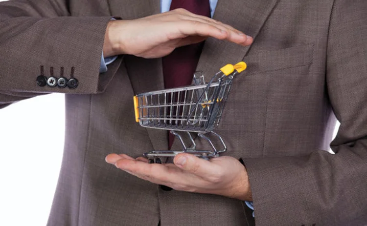 A miniature shopping trolley being cradled in the hands of a suited man
