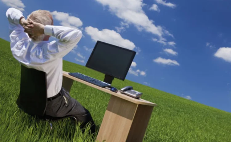 A man using his desktop in a field and looking at clouds