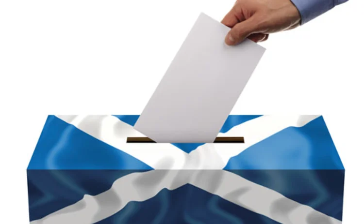 A hand putting a voting slip into a box adorned with the Scottish flag denoting the Scottish independence referendum