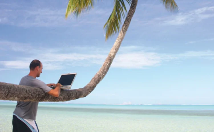 A man working with a laptop on the beach