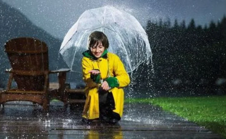 A girl crouching in the rain holding an umbrella