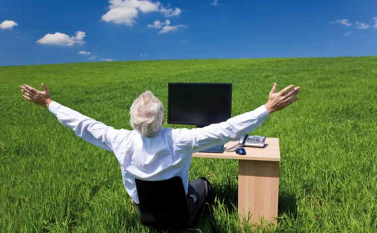 A businessman sat at a desk in a green pasture