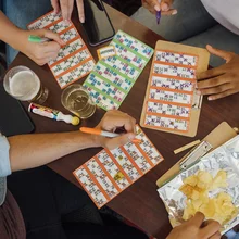 A group of people sitting in a social club enjoying an alcoholic drink while playing a game of bingo together in Newcastle upon Tyne, England. They are all marking numbers off their bingo cards.