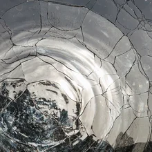 View through a cracked or fractured transparent or translucent glass vase of a back garden. Circles of wavey light ripples distorted and refracted. Background abstract pattern and texture