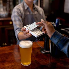 Close-up on a man making a contactless payment at the pub while drinking beer - financial technology concepts