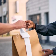 Cheerful courier wearing a helmet and backpack handing over a package to a customer, capturing the essence of efficient delivery service and modern logistics