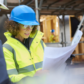 a female construction worker stands on a building site housing development and instructs a co -worker.