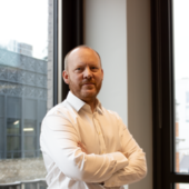 Dan McNally by a window with his arms crossed.
