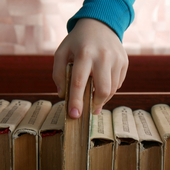 Close-up of a child's hand taking a book from a book shelf
