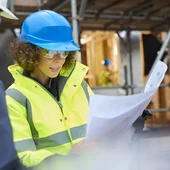 a female construction worker stands on a building site housing development and instructs a co -worker.